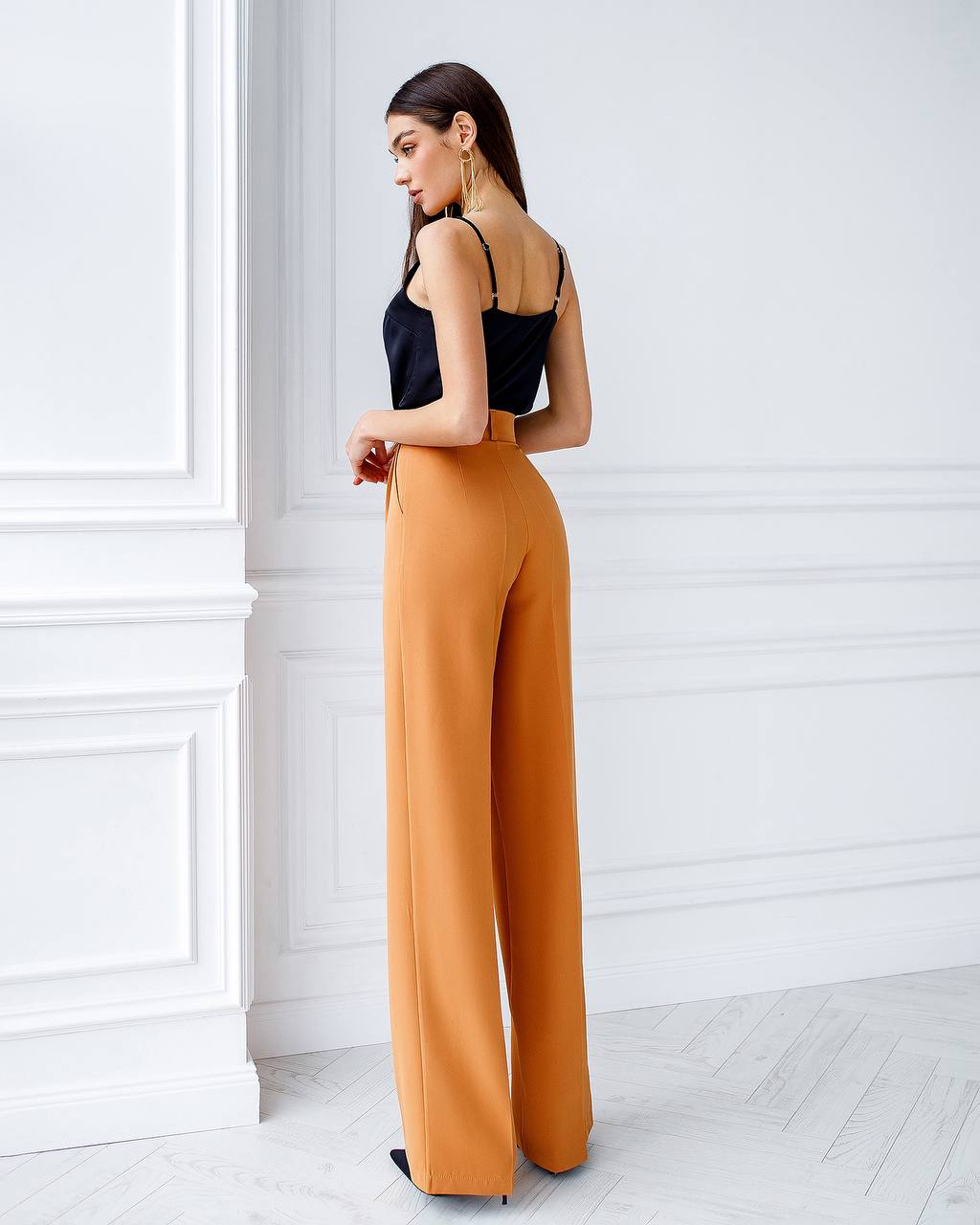 Woman wearing a black top and mustard yellow pants in a minimalistic room.
