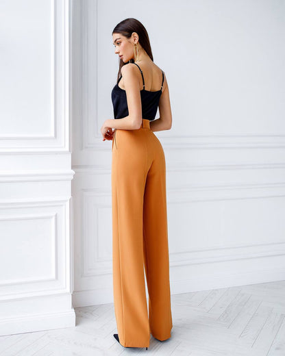 Woman wearing a black top and mustard yellow pants in a minimalistic room.