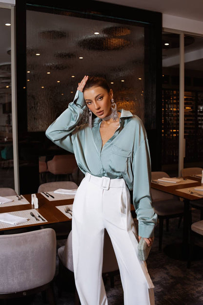 Woman in a light blue shirt and white pants posing in a restaurant.