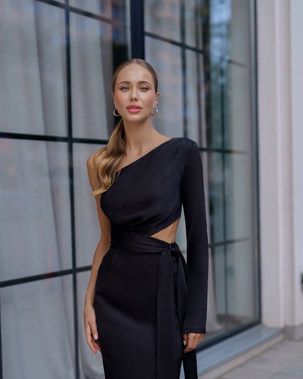 Woman wearing a black one-shoulder dress standing in front of a modern building.