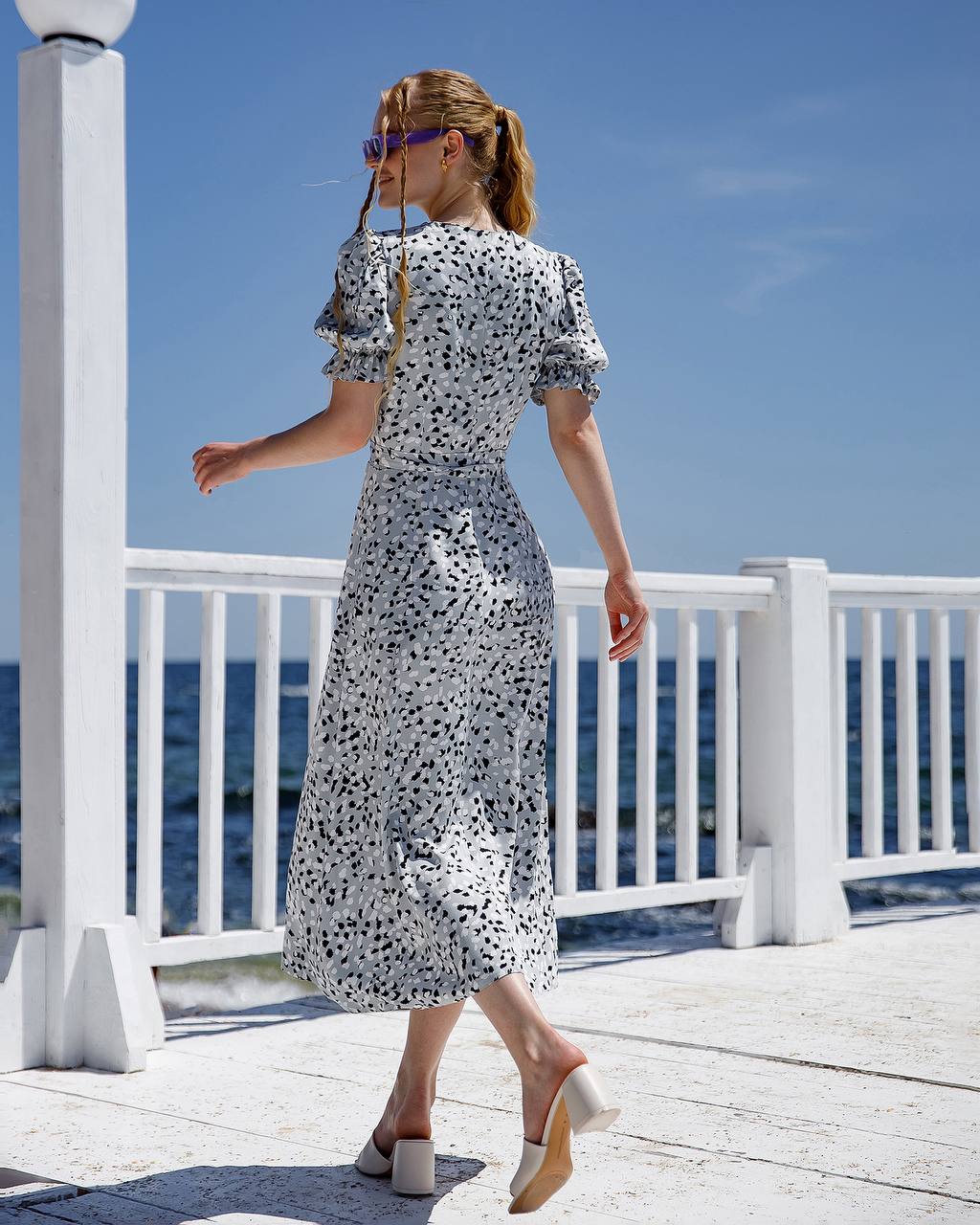 Woman in a floral dress standing on a deck with ocean view