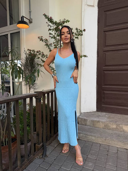 Woman in a light blue dress standing on a porch with plants and a door in the background.