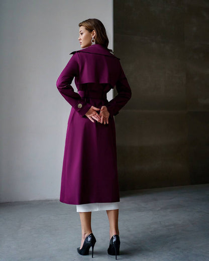 Woman wearing a long purple coat against a plain background