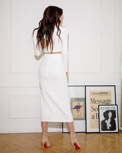 Woman in a white outfit standing in a room with framed pictures on the wall.