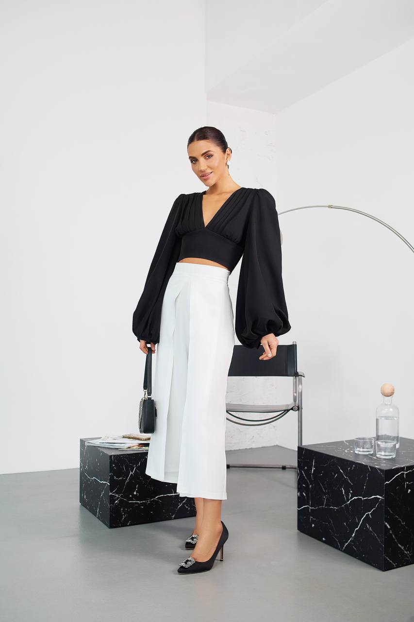 Woman in black top and white pants standing in a modern interior setting.
