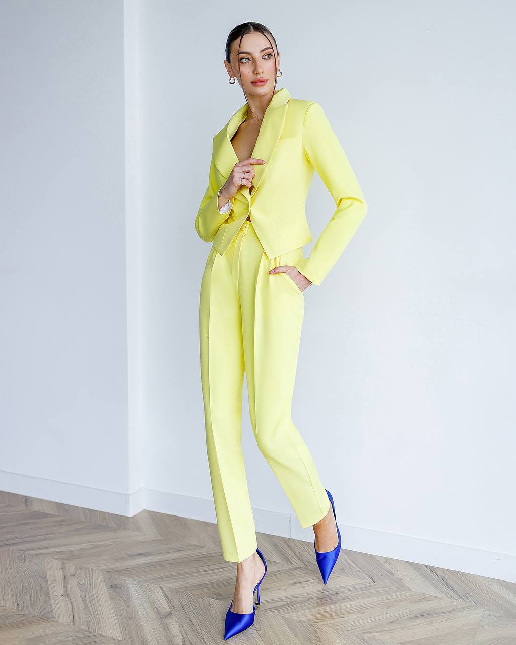 Woman wearing a bright yellow suit with blue shoes on a plain background