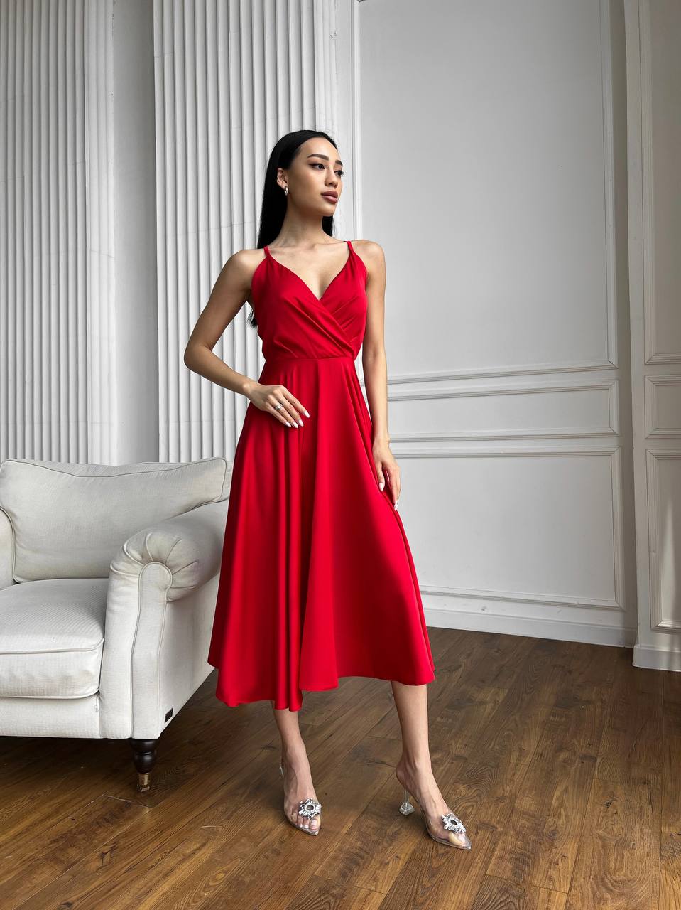 Woman in a red dress standing in a room with white walls and a white sofa.