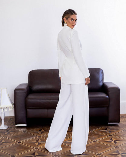 Woman in a white outfit standing in front of a brown leather armchair.