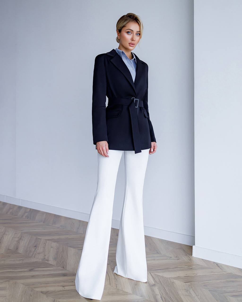 Woman wearing a navy blazer and white pants in a minimalistic setting