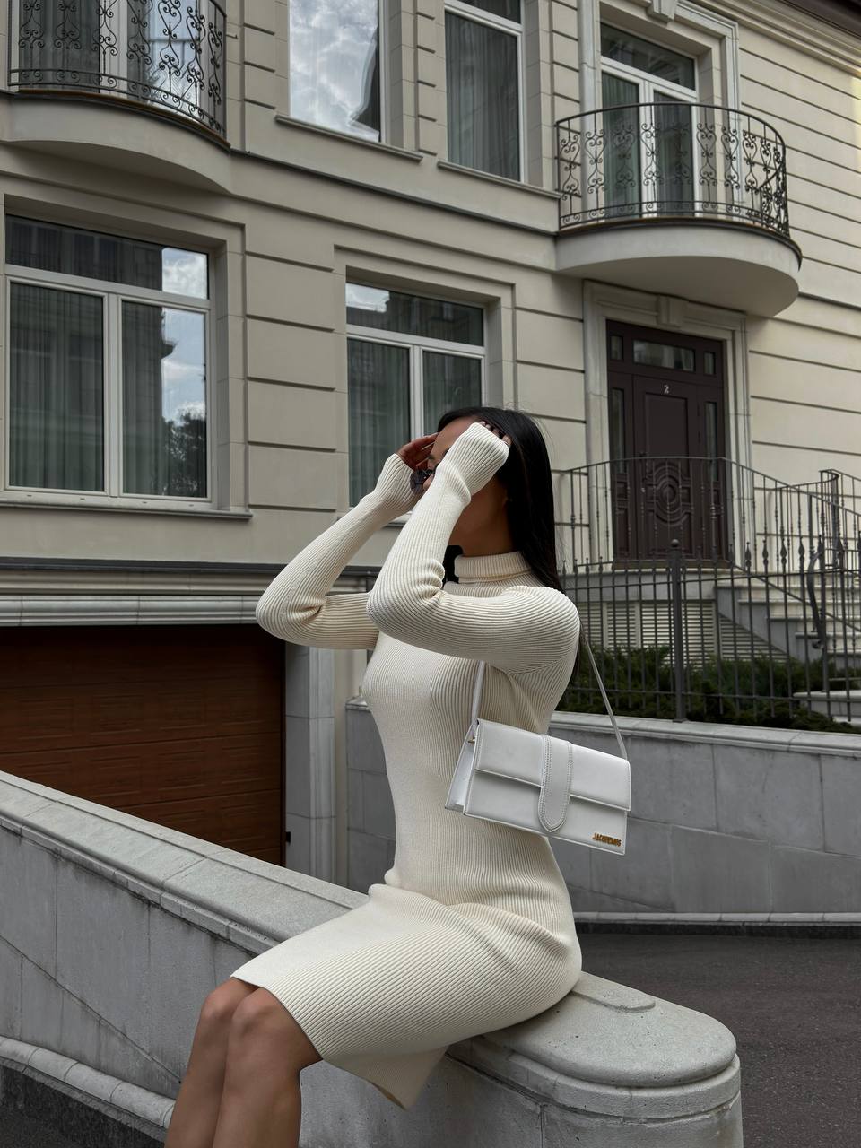Woman in a white outfit sitting on a wall with a building in the background