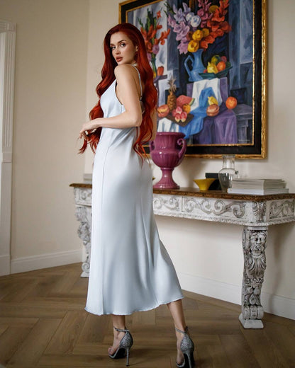 Woman in a light blue dress standing in a room with a decorative table and colorful painting.
