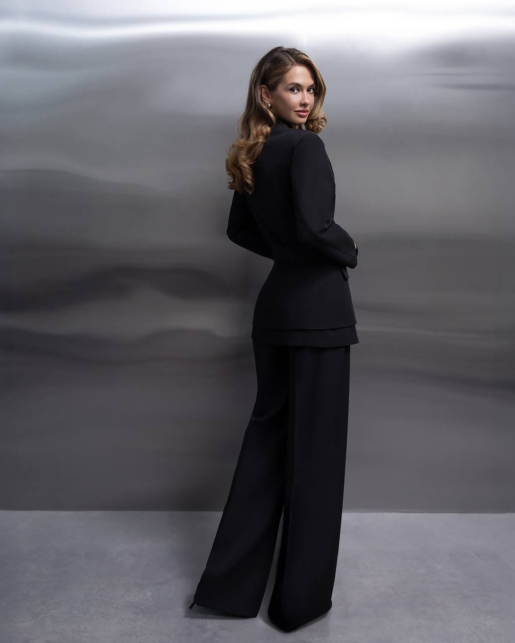 Woman in a black suit standing against a gray background