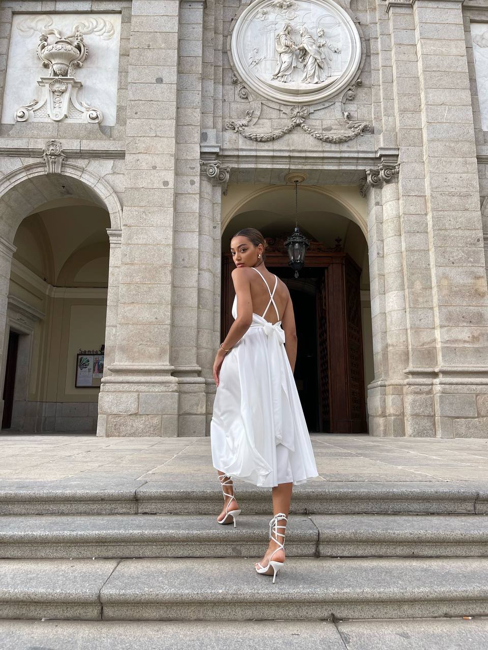 Woman in a white dress standing on steps in front of an ornate building