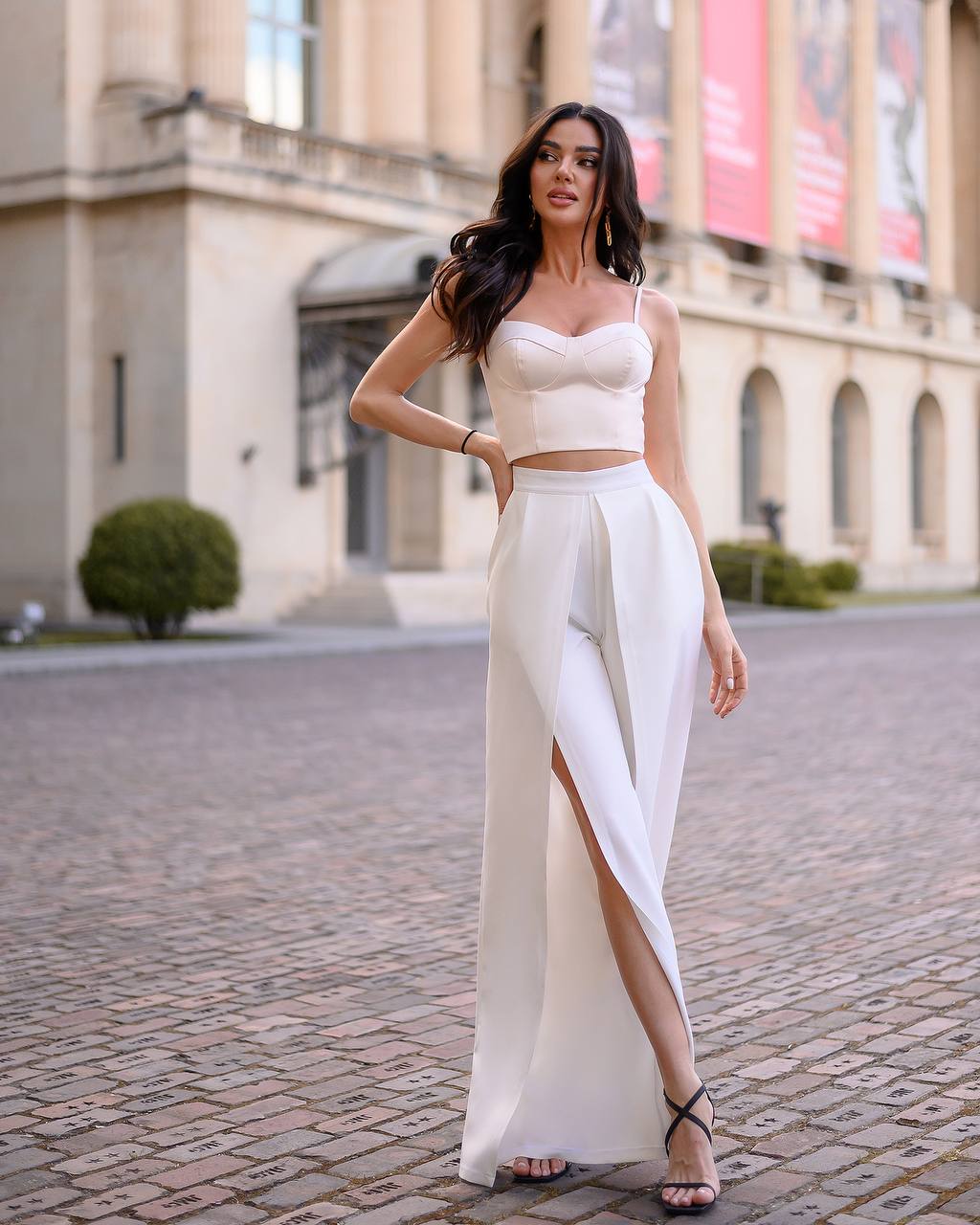 Woman in a white outfit standing on a cobblestone street with classical architecture in the background