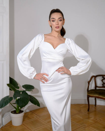 Woman wearing a white dress with long sleeves in an indoor setting.