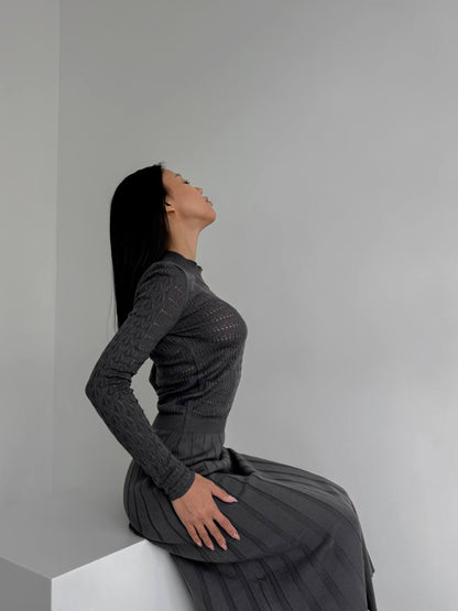 Woman in a gray dress sitting on a white surface against a plain background