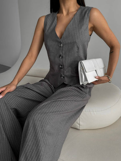 Woman in gray pinstripe suit holding a white clutch against a neutral background