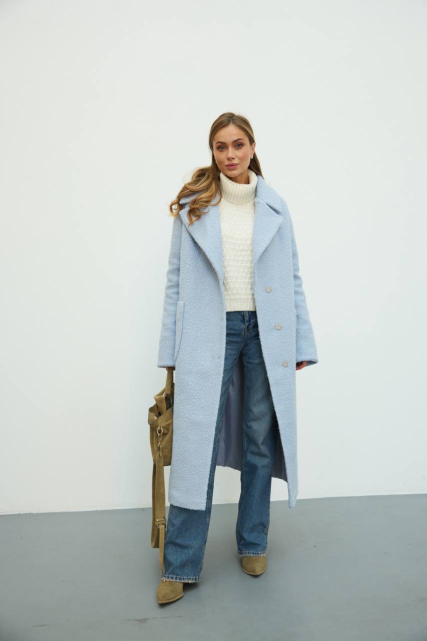 Woman wearing a light blue coat, white sweater, and jeans against a white background