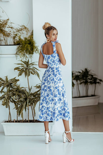 Woman in a blue floral dress standing in a room with plants