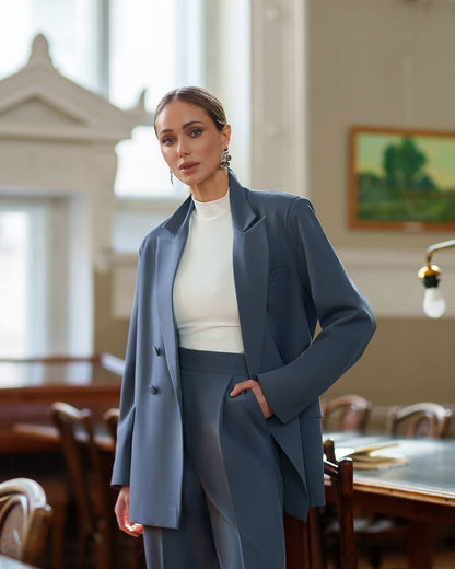Woman in a blue suit standing in an elegant room with large windows.