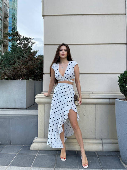 Woman in a polka dot dress standing outdoors near a building.