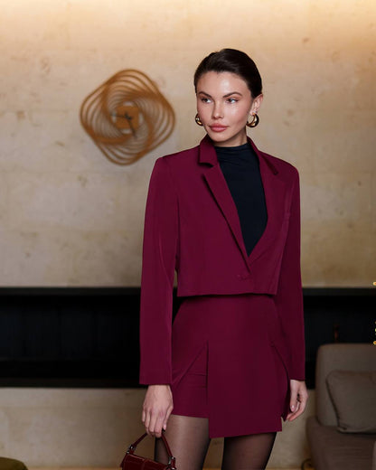 Woman wearing a burgundy suit with a black top in an elegant interior setting.