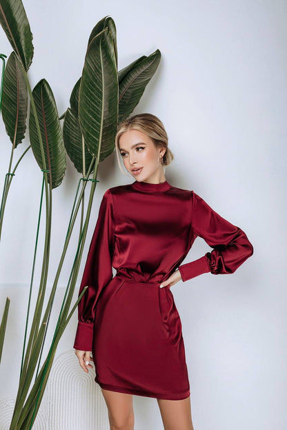 Woman wearing a red dress standing next to a plant against a white wall