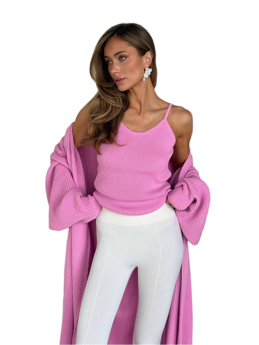 Woman wearing a pink ribbed top and white pants with a pink cardigan on a white background