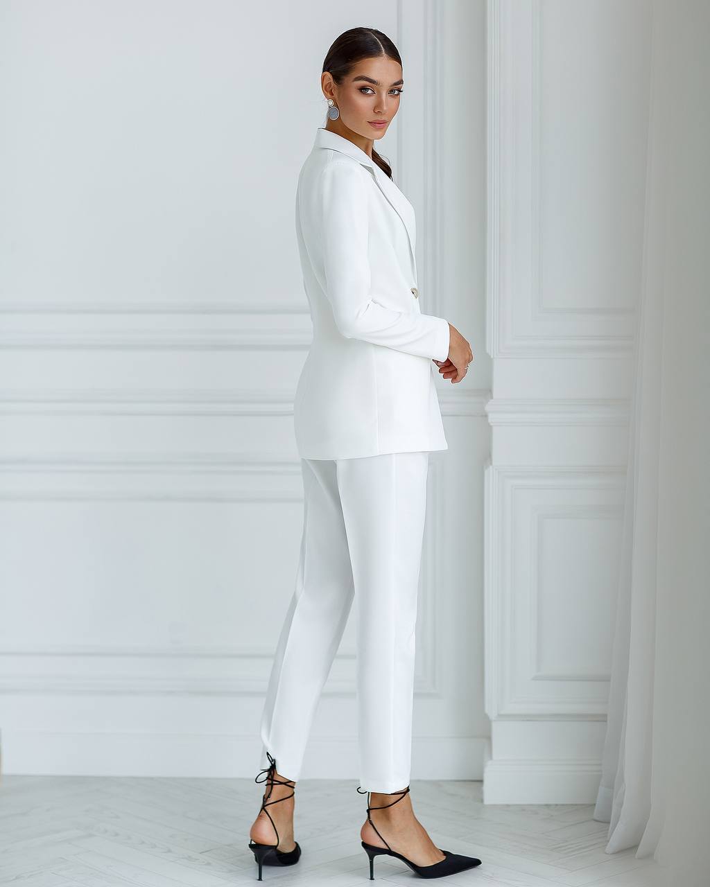 Woman wearing a white suit standing against a white wall.