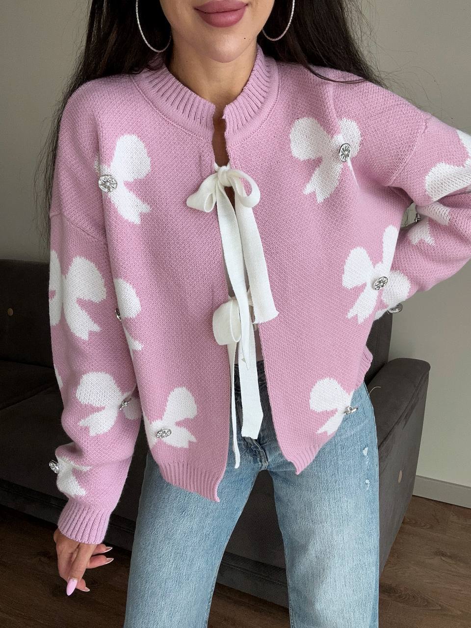 Person wearing a pink sweater with white floral patterns and ribbons.