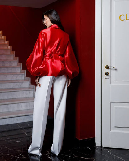 Person wearing a red satin jacket and white pants in a room with a red wall and white door.