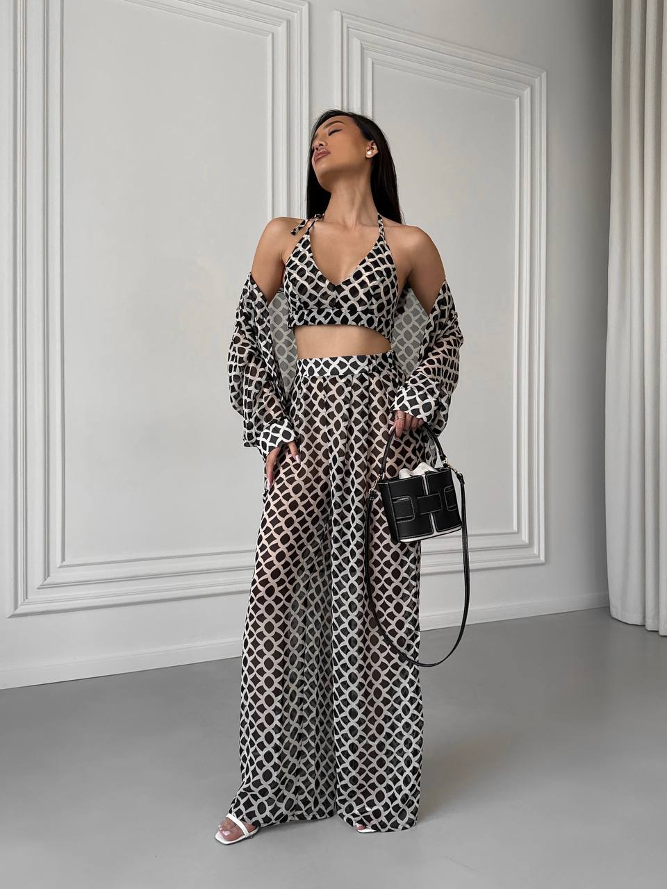 Woman in a black and white patterned outfit standing against a white paneled wall.