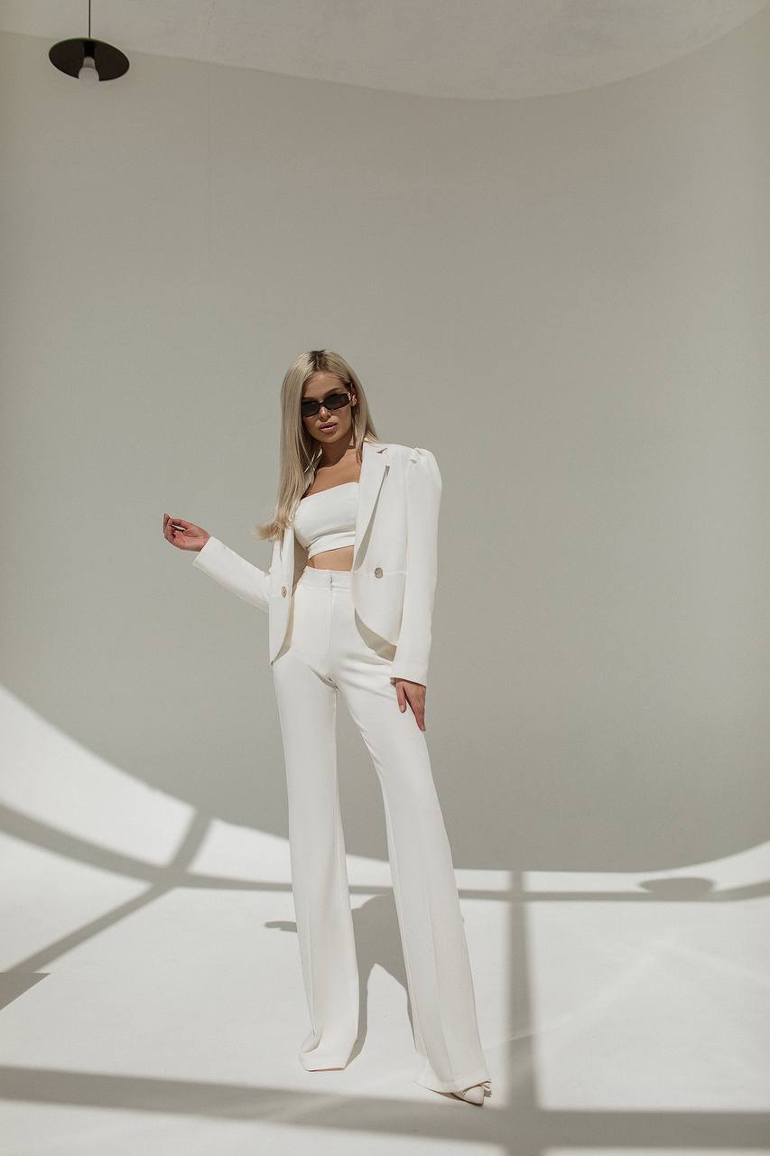 Woman in a white outfit standing in a well-lit room with a neutral background