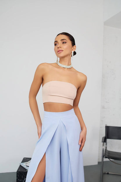 Woman wearing a beige strapless top and light blue skirt with a white background