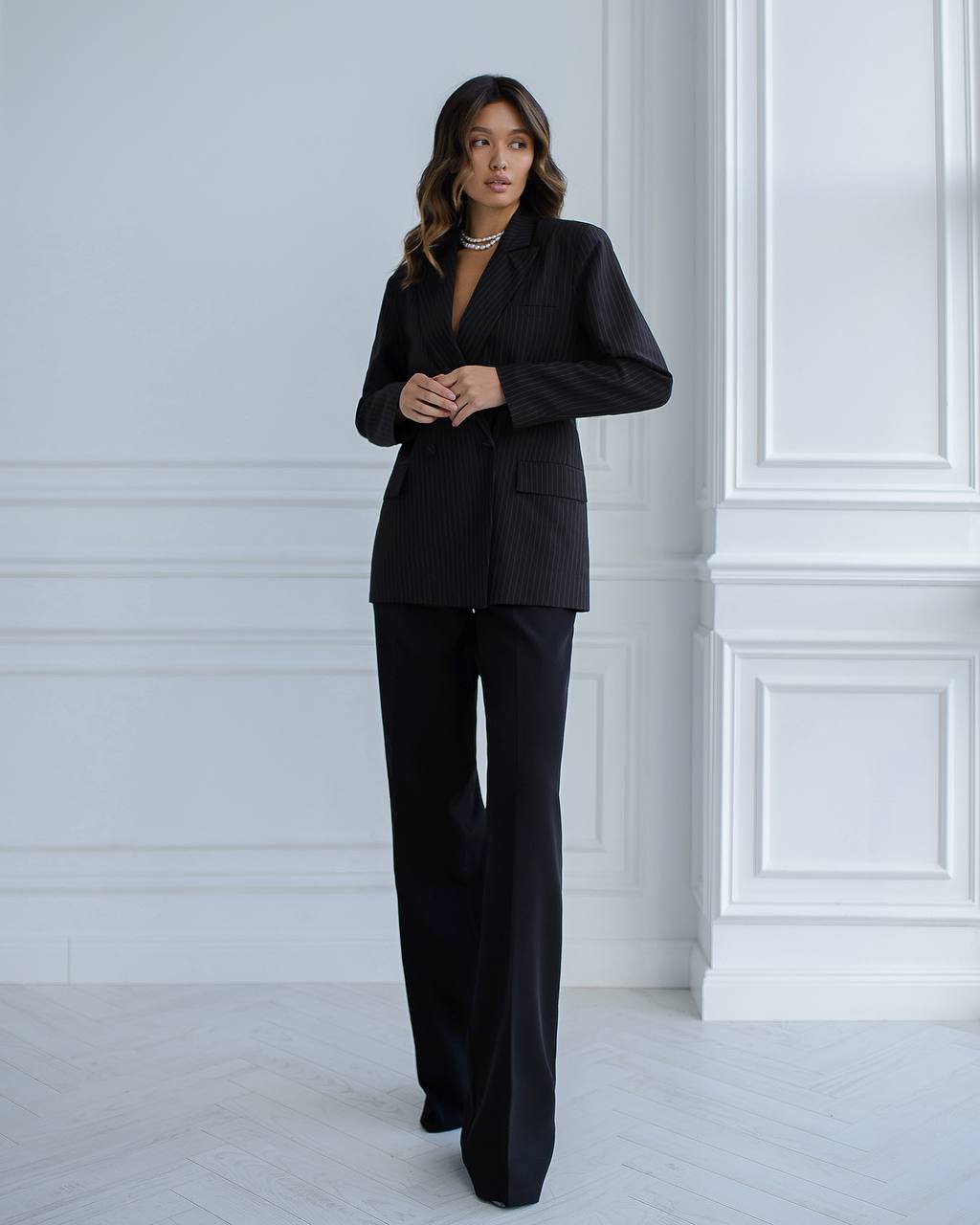 Woman wearing a black suit standing against a white wall.