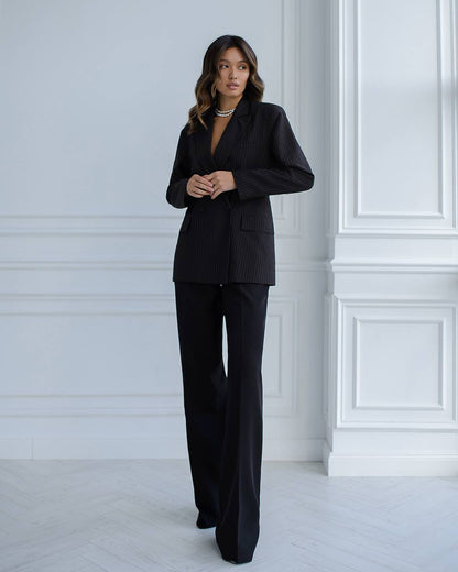 Woman wearing a black suit standing against a white wall.