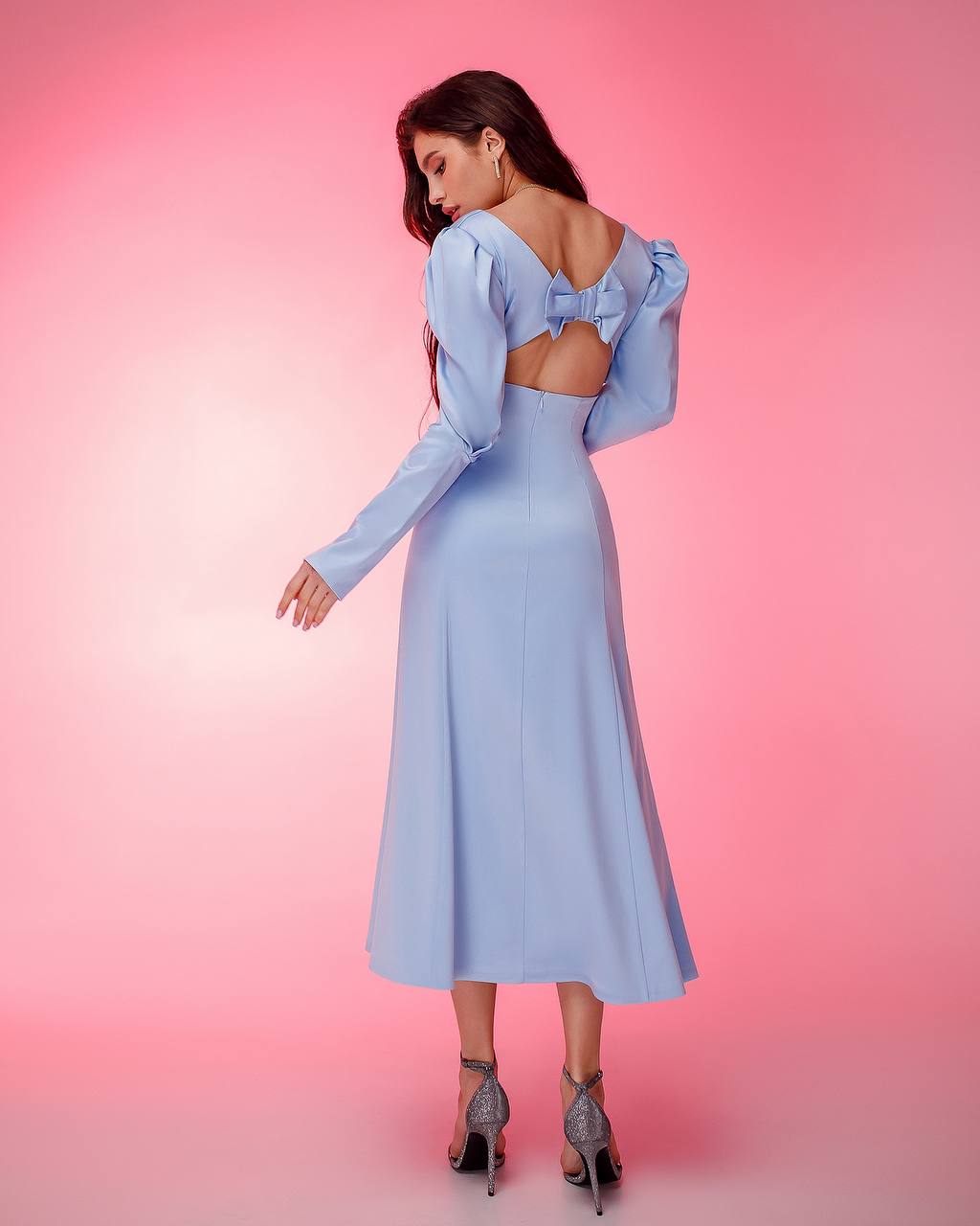 Woman wearing a light blue dress with long sleeves and a bow detail on a pink background