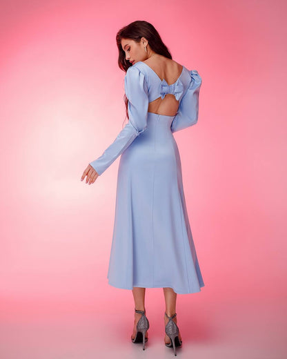 Woman wearing a light blue dress with long sleeves and a bow detail on a pink background