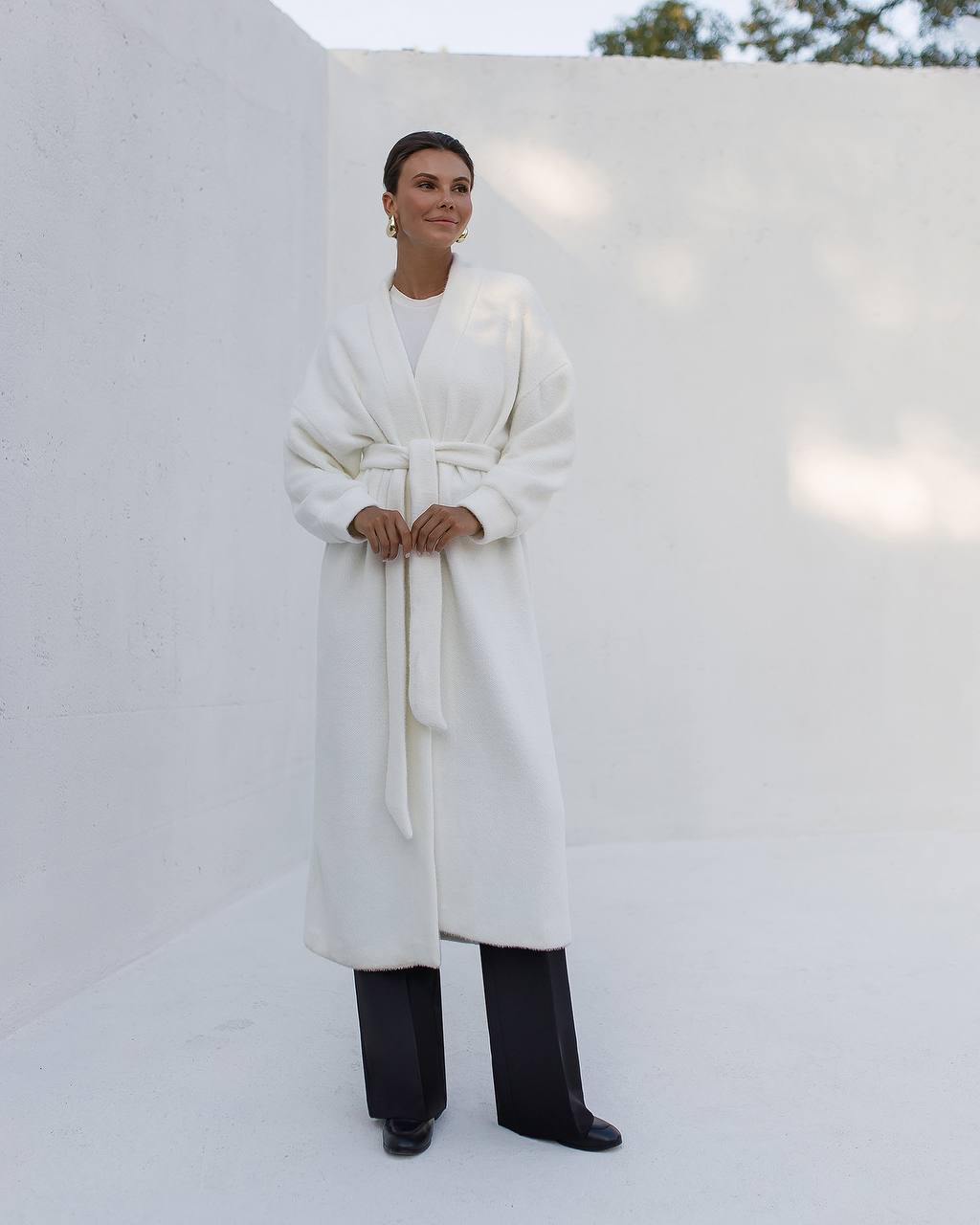 Person wearing a long white coat in a minimalistic setting