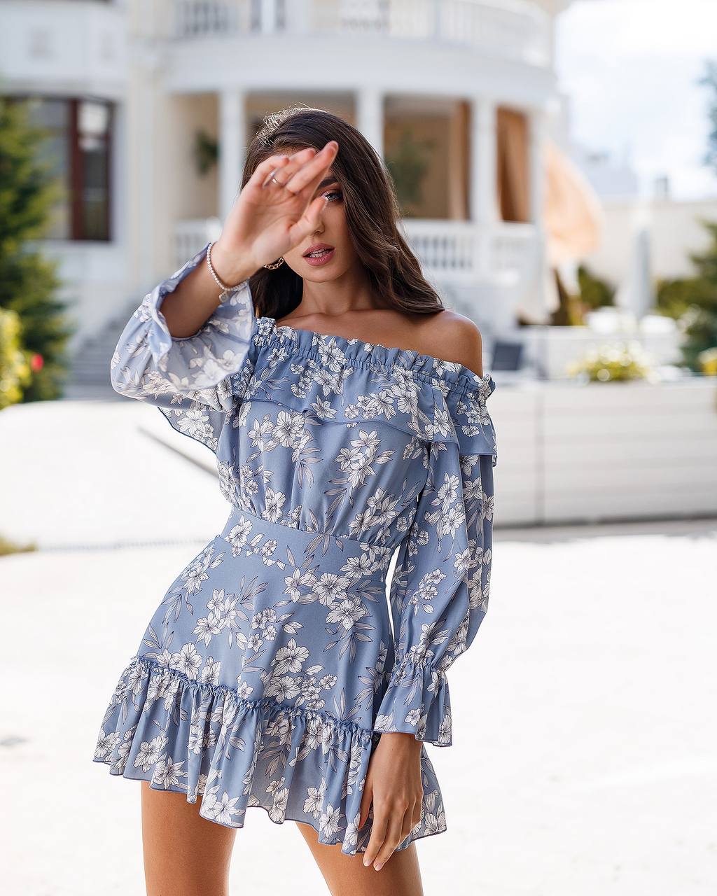 Woman wearing a blue floral off-shoulder dress in front of a white building.