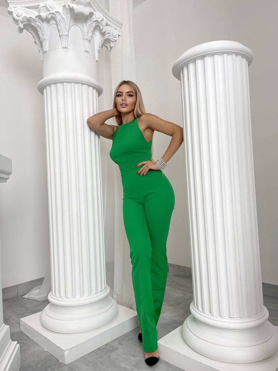 Woman in a green jumpsuit posing between two white columns.