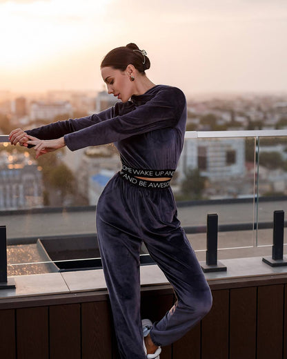 Woman in a navy tracksuit with text standing on a rooftop at sunset.