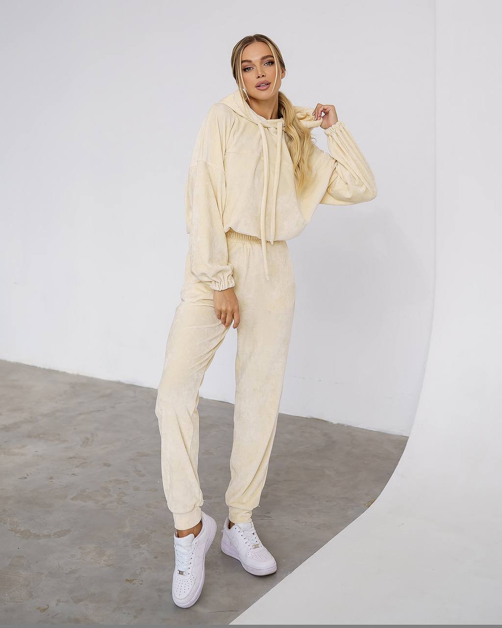 Person wearing a beige tracksuit with white sneakers on a plain background