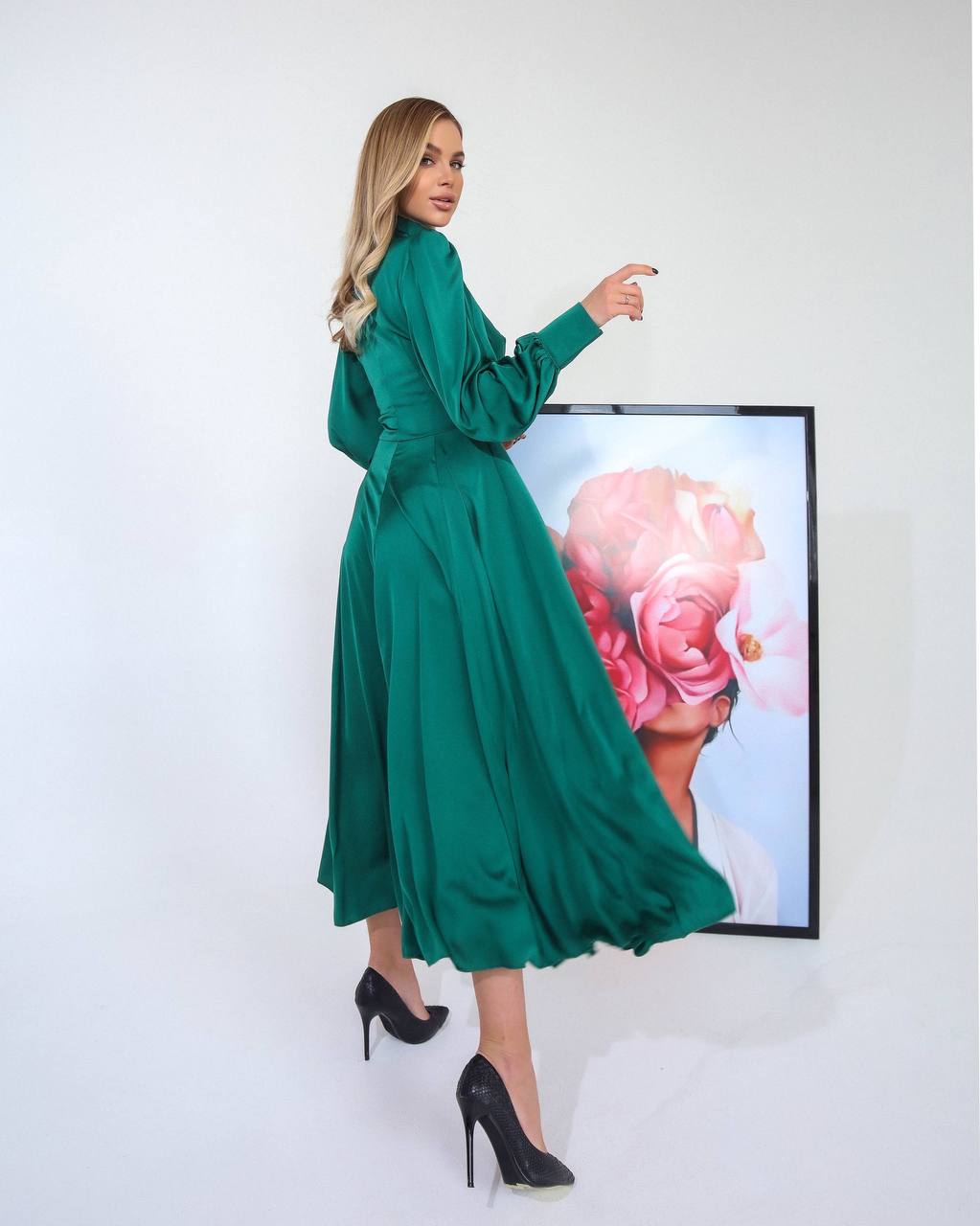Woman in a green dress standing next to a framed artwork on a white wall