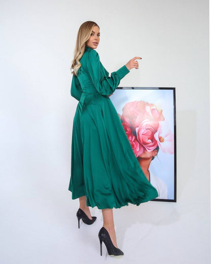 Woman in a green dress standing next to a framed artwork on a white wall
