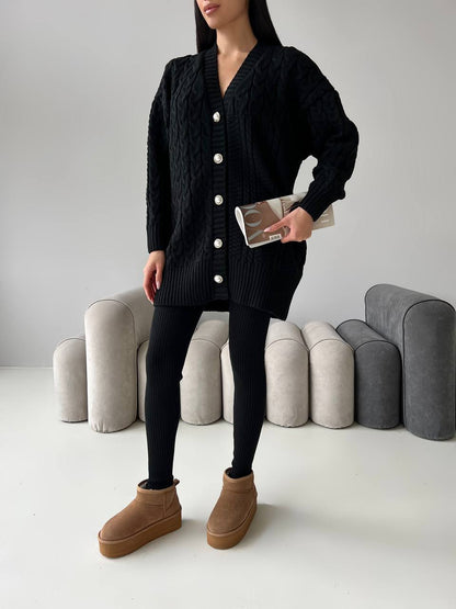 Person wearing a black cardigan, black leggings, and brown boots against a neutral background
