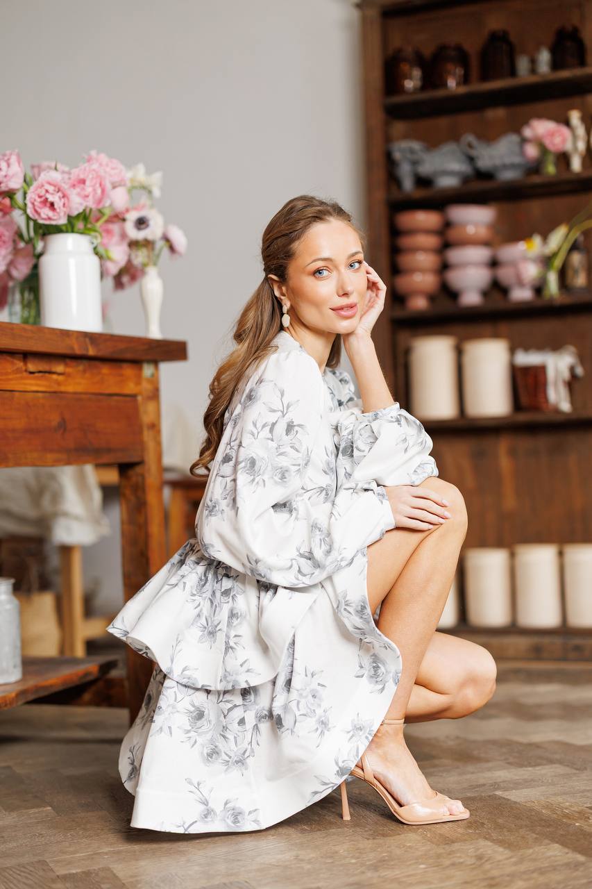 Woman in a floral robe sitting on the floor with a wooden shelf and flowers in the background