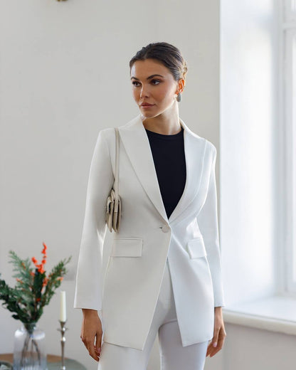 Woman wearing a white blazer and black top in a room with a window and plant.