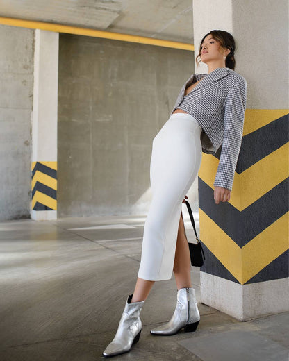 Woman in a gray patterned top, white pants, and silver boots standing in an urban setting.
