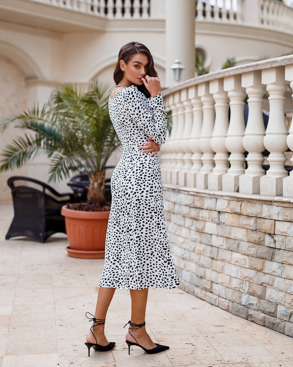 Woman in a polka dot dress standing on a balcony with decorative elements.